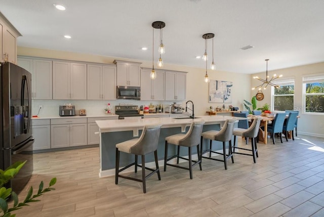 kitchen featuring a breakfast bar, decorative light fixtures, an island with sink, gray cabinetry, and black appliances