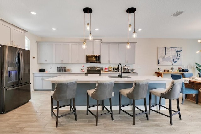 kitchen with hanging light fixtures, black appliances, a kitchen island with sink, and light countertops