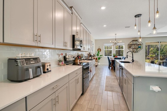 kitchen with sink, double oven range, tasteful backsplash, a center island with sink, and decorative light fixtures