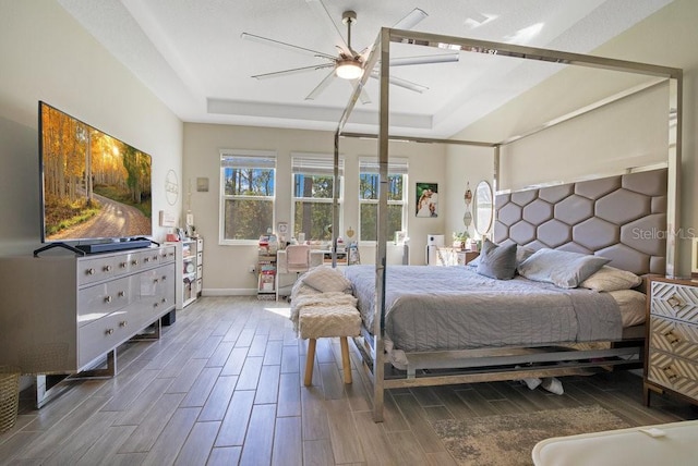 bedroom with baseboards, a tray ceiling, ceiling fan, and wood finish floors