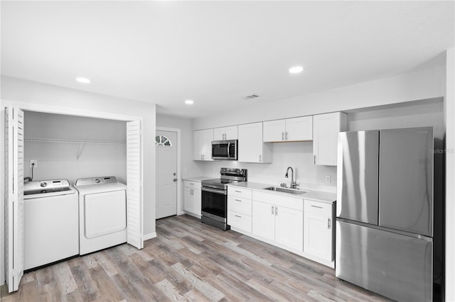 kitchen featuring sink, light wood-type flooring, stainless steel appliances, washer and clothes dryer, and white cabinets