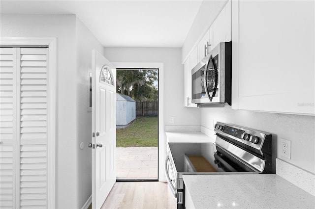 kitchen with white cabinetry, appliances with stainless steel finishes, light stone countertops, and light hardwood / wood-style floors