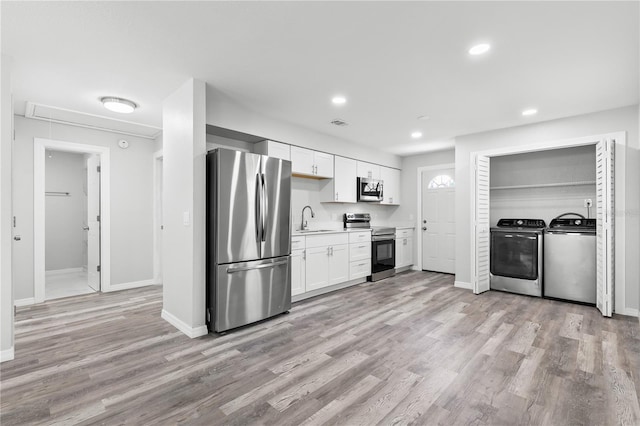 kitchen with sink, light hardwood / wood-style flooring, appliances with stainless steel finishes, independent washer and dryer, and white cabinets