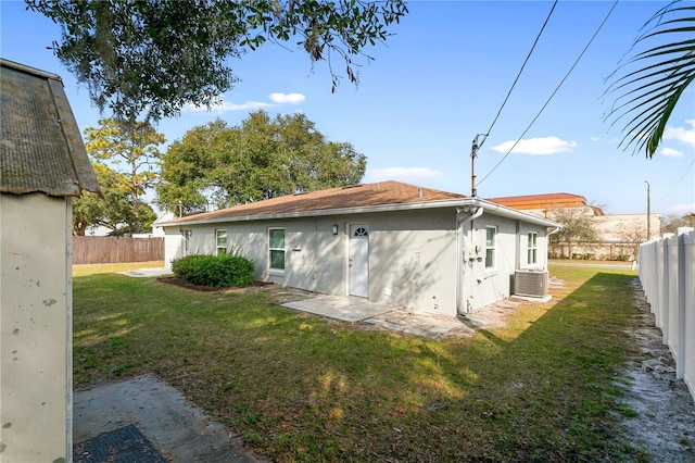 rear view of property featuring central AC unit and a lawn