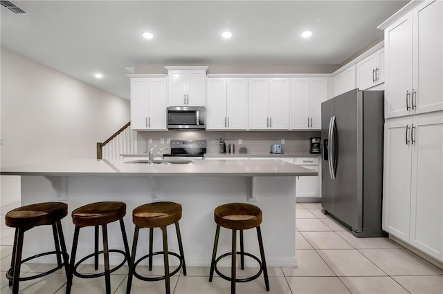 kitchen featuring visible vents, decorative backsplash, a kitchen breakfast bar, stainless steel appliances, and light tile patterned flooring