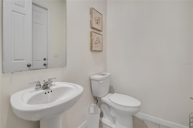 half bathroom with baseboards, a sink, and toilet