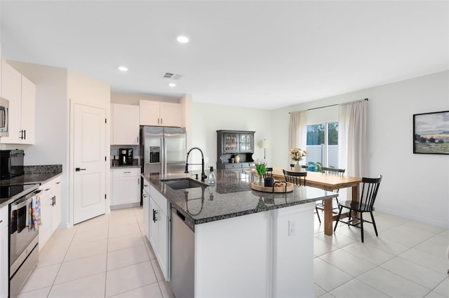 kitchen with sink, stainless steel appliances, white cabinets, a center island with sink, and dark stone counters