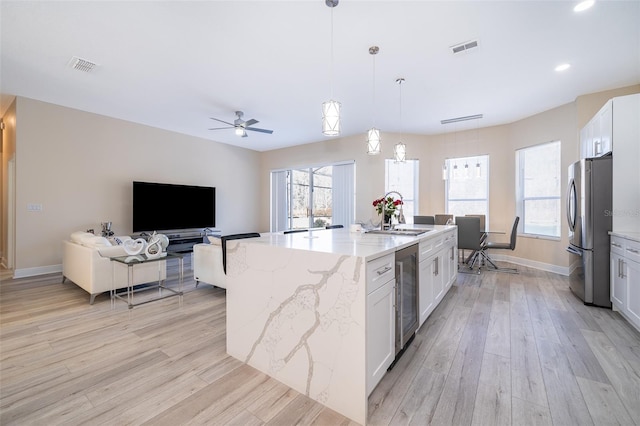 kitchen with pendant lighting, stainless steel refrigerator, white cabinetry, light stone countertops, and beverage cooler