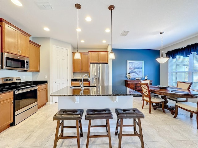 kitchen with sink, dark stone counters, an island with sink, pendant lighting, and stainless steel appliances