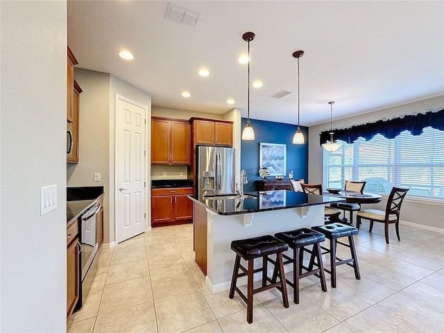 kitchen featuring a center island with sink, stainless steel appliances, a kitchen bar, decorative light fixtures, and light tile patterned flooring