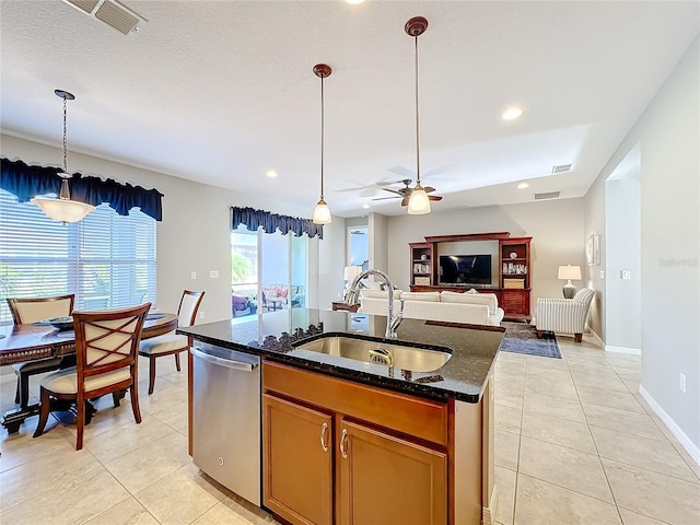 kitchen featuring dishwasher, sink, dark stone countertops, hanging light fixtures, and a kitchen island with sink