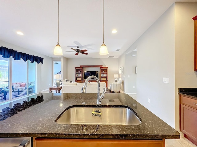 kitchen featuring hanging light fixtures, sink, ceiling fan, and dark stone counters