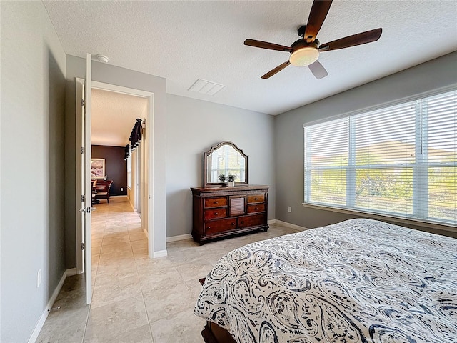 bedroom with ceiling fan, light tile patterned floors, and a textured ceiling