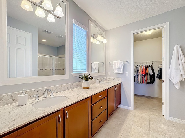 bathroom with a shower with door, vanity, tile patterned flooring, and a textured ceiling