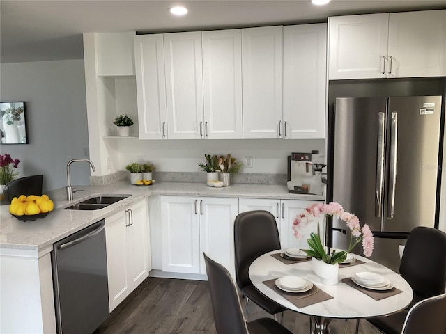 kitchen with sink, dark wood-type flooring, appliances with stainless steel finishes, light stone counters, and white cabinets