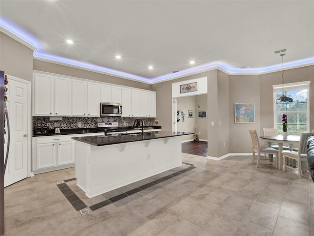 kitchen with a kitchen island with sink, a sink, appliances with stainless steel finishes, dark countertops, and a raised ceiling