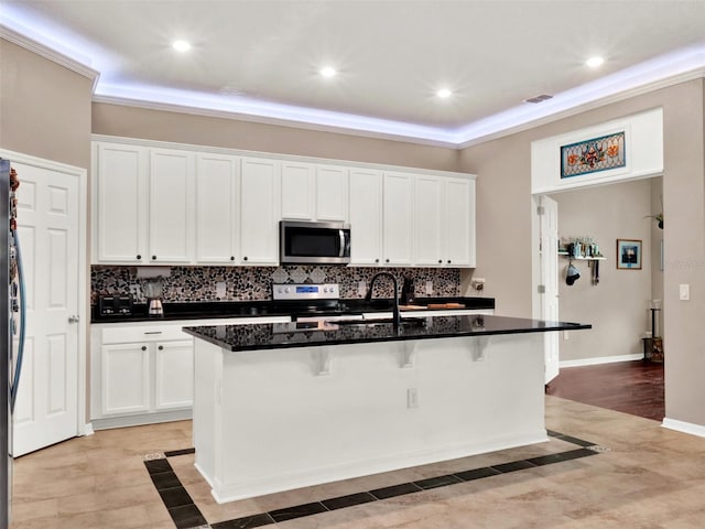 kitchen with appliances with stainless steel finishes, a breakfast bar, white cabinets, and tasteful backsplash