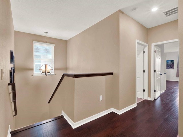 hallway with baseboards, visible vents, wood finished floors, an upstairs landing, and a notable chandelier