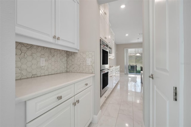 kitchen featuring white cabinetry, stainless steel double oven, and backsplash