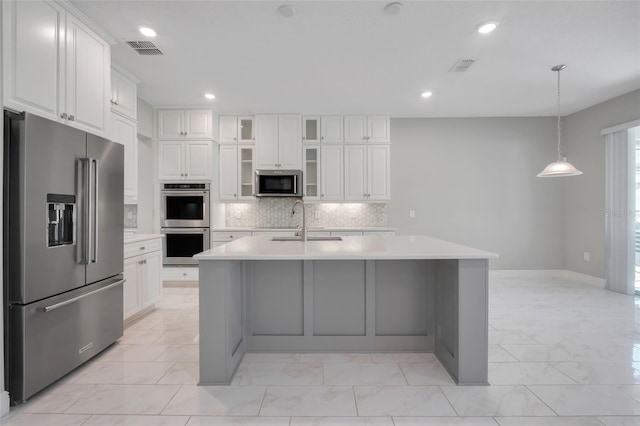 kitchen featuring pendant lighting, tasteful backsplash, white cabinets, a kitchen island with sink, and stainless steel appliances