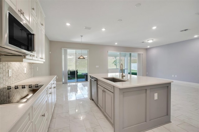 kitchen with pendant lighting, sink, stainless steel appliances, white cabinets, and a center island with sink