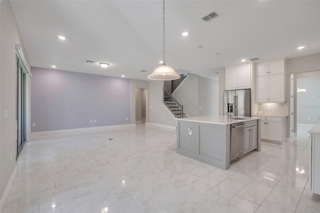 kitchen with backsplash, stainless steel appliances, an island with sink, white cabinets, and decorative light fixtures