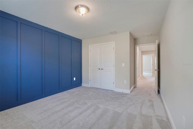 unfurnished bedroom with light colored carpet, a closet, and a textured ceiling