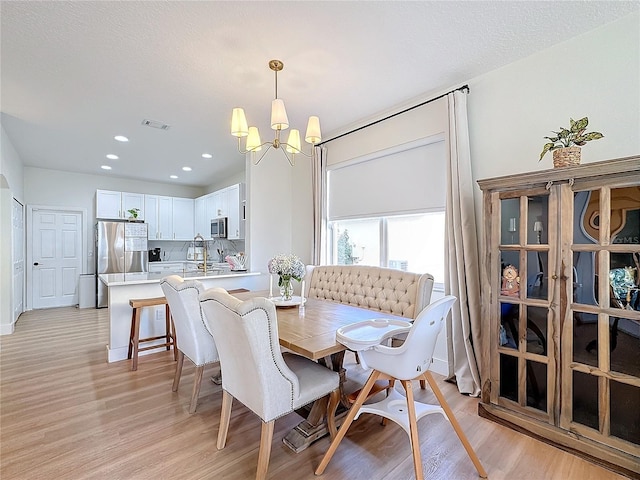 dining space featuring an inviting chandelier, light hardwood / wood-style flooring, and a textured ceiling