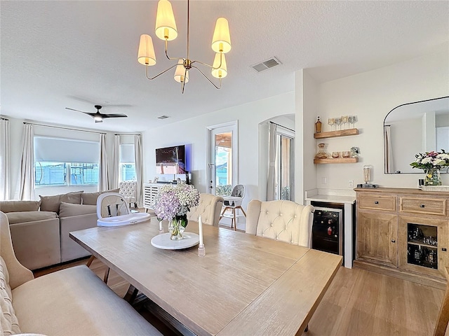 dining room featuring light hardwood / wood-style flooring, beverage cooler, a textured ceiling, and plenty of natural light