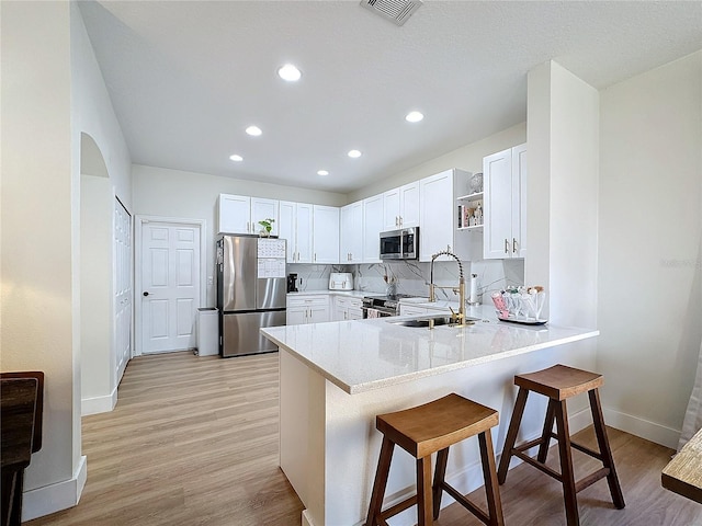 kitchen featuring a kitchen bar, sink, white cabinetry, tasteful backsplash, and stainless steel appliances