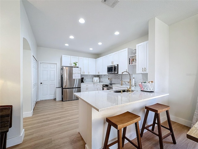 kitchen with sink, a breakfast bar area, stainless steel appliances, white cabinets, and decorative backsplash