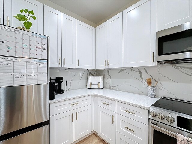 kitchen with light stone counters, backsplash, white cabinets, and appliances with stainless steel finishes