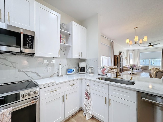 kitchen with appliances with stainless steel finishes, sink, white cabinets, backsplash, and hanging light fixtures