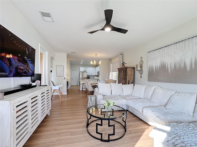 living room with ceiling fan with notable chandelier, light hardwood / wood-style floors, and a textured ceiling