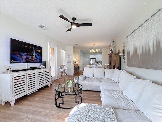 living room with ceiling fan with notable chandelier, a textured ceiling, and light hardwood / wood-style floors