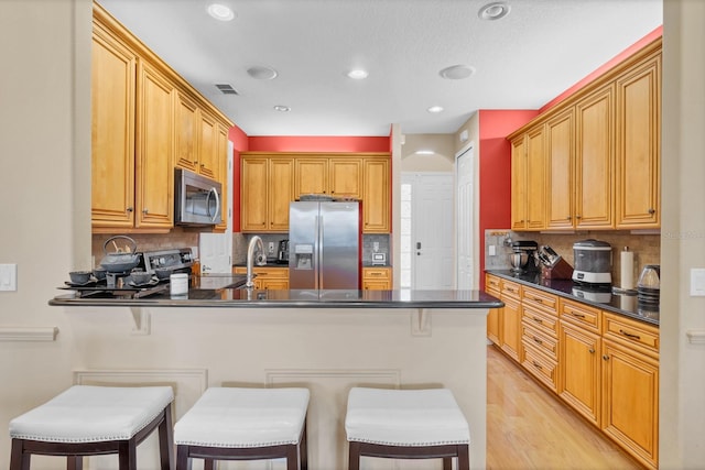 kitchen with stainless steel appliances, kitchen peninsula, a breakfast bar area, and light wood-type flooring