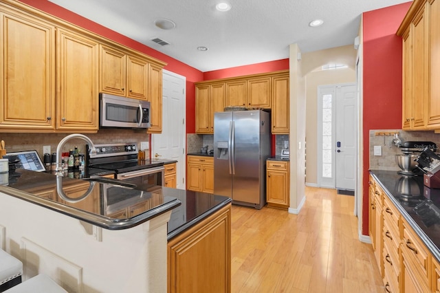 kitchen with light wood-type flooring, appliances with stainless steel finishes, a kitchen breakfast bar, kitchen peninsula, and decorative backsplash