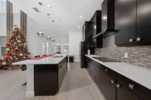 kitchen featuring pendant lighting, an island with sink, sink, black appliances, and wall chimney exhaust hood