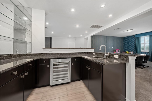 kitchen with sink, kitchen peninsula, wine cooler, and dark stone counters