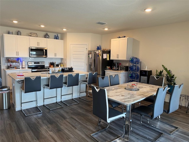 kitchen featuring appliances with stainless steel finishes, white cabinetry, backsplash, a center island with sink, and dark hardwood / wood-style flooring