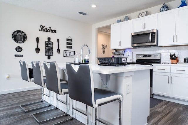 kitchen featuring an island with sink, appliances with stainless steel finishes, white cabinets, and a kitchen bar