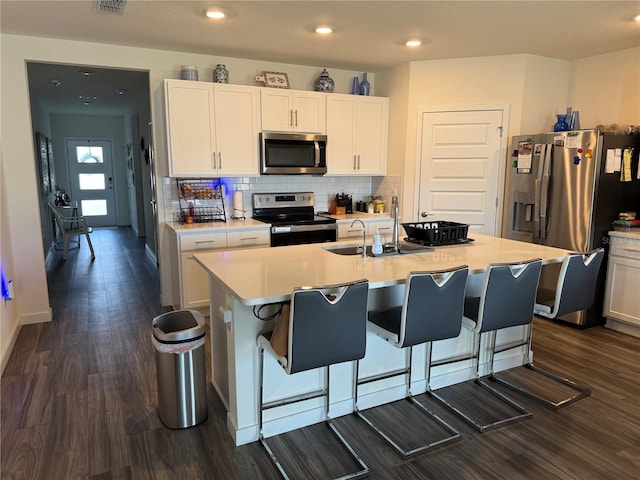 kitchen with dark wood finished floors, light countertops, backsplash, appliances with stainless steel finishes, and white cabinets