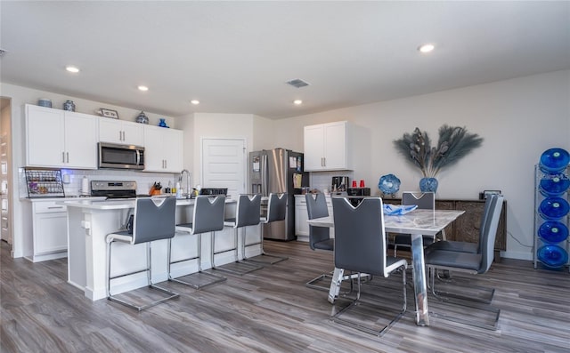 kitchen featuring dark wood-style floors, stainless steel appliances, an island with sink, and white cabinets