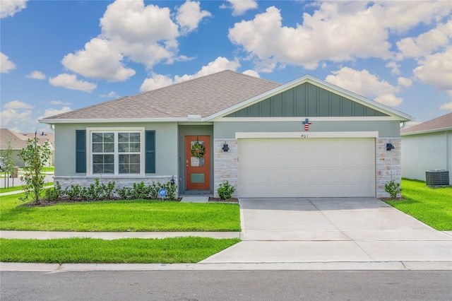 view of front of house with an attached garage, a front yard, central AC, stone siding, and driveway