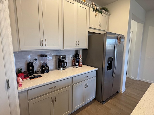 kitchen featuring light stone countertops, hardwood / wood-style floors, backsplash, and stainless steel fridge with ice dispenser