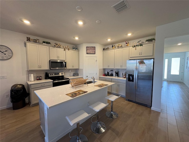 kitchen featuring a breakfast bar, stainless steel appliances, a center island with sink, dark hardwood / wood-style flooring, and decorative backsplash