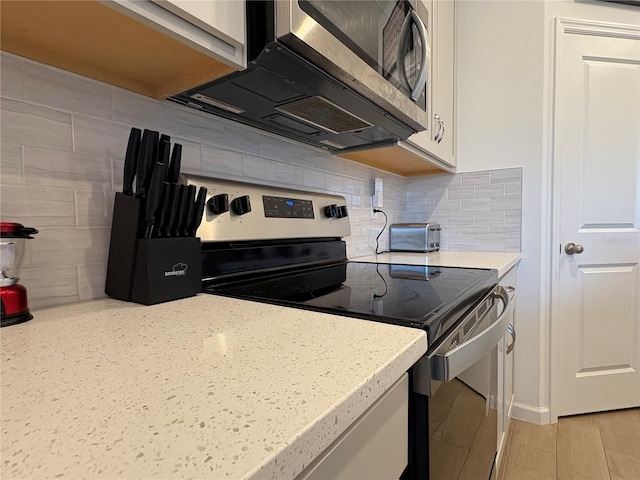 kitchen featuring backsplash, light wood-type flooring, white cabinets, and appliances with stainless steel finishes