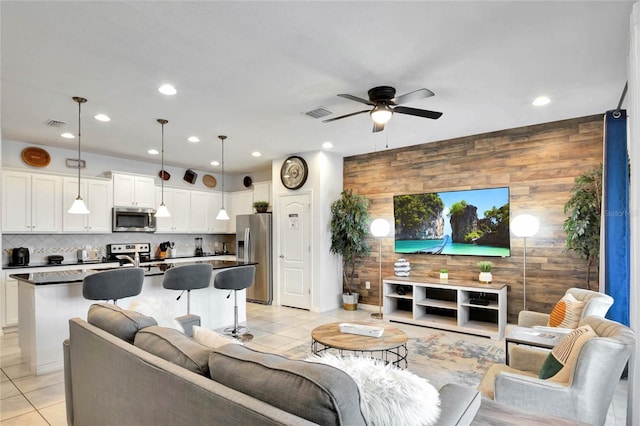 living room with light tile patterned flooring, ceiling fan, and wooden walls