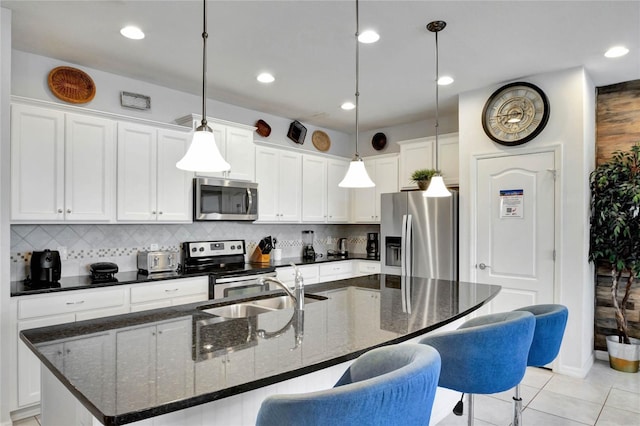 kitchen featuring appliances with stainless steel finishes, decorative light fixtures, white cabinetry, dark stone countertops, and a center island with sink