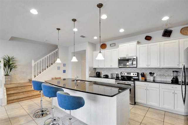 kitchen with sink, a kitchen island with sink, white cabinetry, stainless steel appliances, and decorative light fixtures